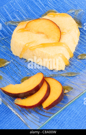 Heart shaped peach bavarian cream dessert with peach sauce and peach slices on a transparent glass plate over a blue background. Stock Photo