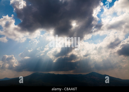 Broken rain clouds with blue sky and sun streaming through clouds and hills Stock Photo