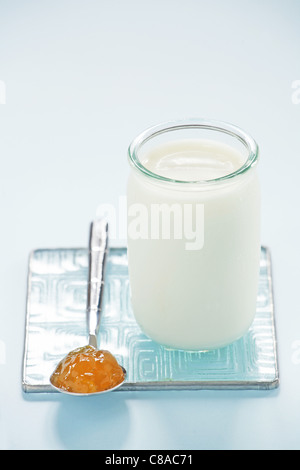 Plain yoghurt in a glass pot and a spoonful of jam Stock Photo