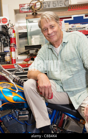 Portrait of senior man sitting on motorcycle in workshop Stock Photo