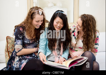 Young women looking at magazines on a sofa Stock Photo