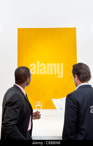 Two people looking at yellow painting on wall in art gallery Stock Photo