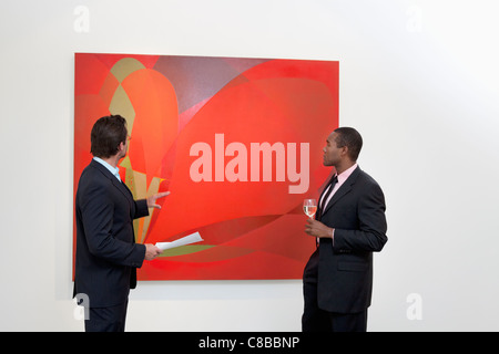 Two males talking over painting in art gallery Stock Photo