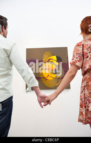 Married couple holding hands in front of painting in art gallery Stock Photo