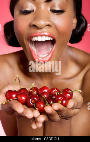 Cheerful young woman looking at cherry in her hands Stock Photo