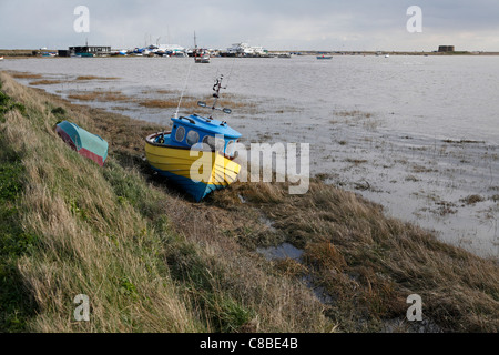 little yellow and blue fishing boat abandoned on the bank of the River Alde at Slaughden, near Aldeburgh, Suffolk, UK Stock Photo