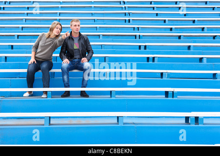 Man and woman sitting together on empty sports tribune along. Only two people on blue chairs Stock Photo