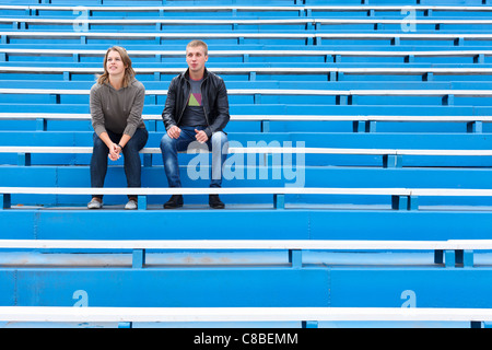 Man and woman sitting together on empty sports tribune along. Only two people on blue chairs Stock Photo