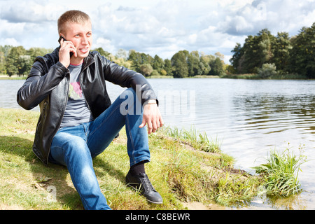 Handsome man sitting near river and calling on mobile phone. Russian nature and people Stock Photo