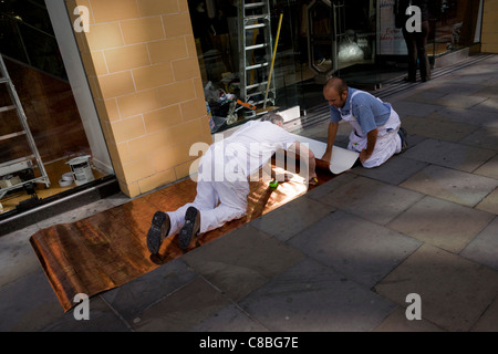 Two workmen measure and fit a shop window design backing for a high-street London retailer. Stock Photo
