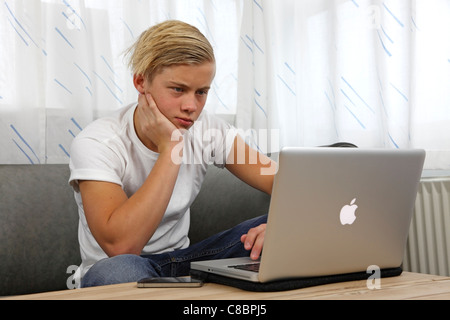 Teenager using his Apple MacBook Pro for homework while keeping his friends up-to-date on the social networking services Stock Photo