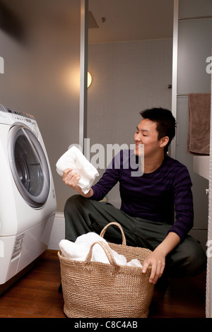 Young man holding and looking at towel in front of laundry machine Stock Photo