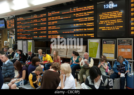 Passengers waiting beneath a passenger information board at Kings Cross railway Station in London. Stock Photo