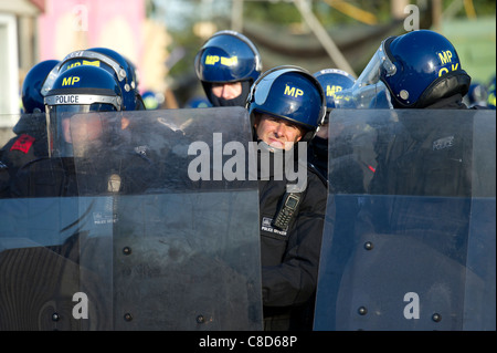 A line of riot police block the road with shields as one officer peers around his shield at the Dale Farm traveller eviction. Stock Photo