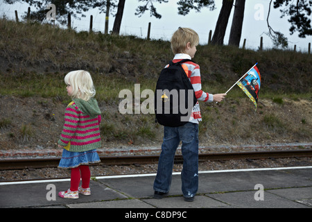Waiting train children. Older brother and younger sister wait patiently at the station platform for the arrival of Thomas the Tank Engine. England UK Stock Photo