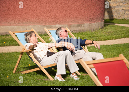 Senior couple hand in hand resting on deckchairs. Stock Photo