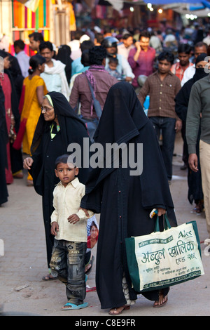 Street scene in holy city of Varanasi, muslim woman in black veil burkha shopping with her child, India Stock Photo