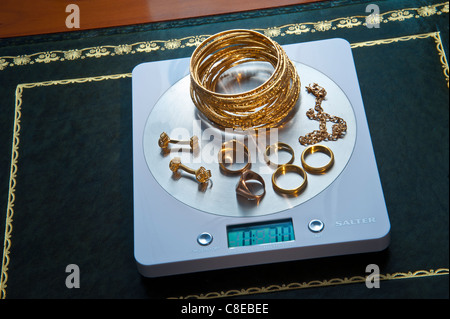 Weighing selection of solid 22ct gold jewellery on portable digital desk weighing machine displaying weight in ounces Stock Photo