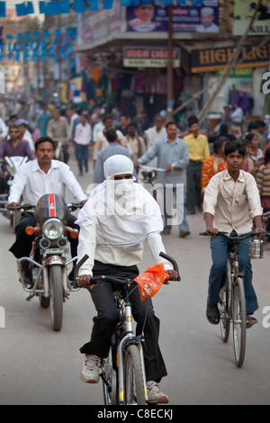 Muslim woman with hijab burkha veil covering head and face cycles in the street in city of Varanasi, Benares, Northern India Stock Photo