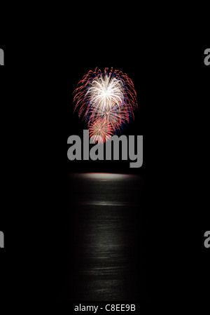 red white and blue fireworks with water below and black background Stock Photo