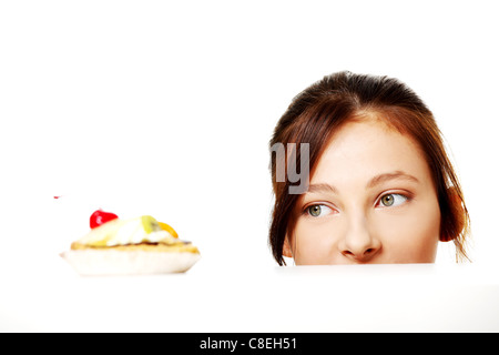 Young caucasian girl hiding behind the desk and looking at the cake over white.  Stock Photo