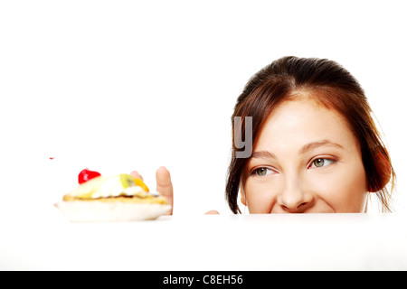 Young caucasian girl hiding behing the desk and reaching for the cake over white.  Stock Photo