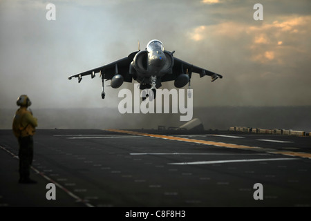 As a crewmember of USS Essex (LHD 2) looks on, an AV-8B Harrier lands on the flight deck Stock Photo
