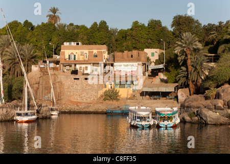 late afternoon shot of feluccas and water taxis moored in front of a small village on the river Nile, reflected in calm water Stock Photo