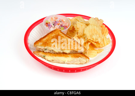 Toasted tunamelt sandwich with coleslaw and potato chips on white paper plate in red plastic basket on white background cutout. Stock Photo