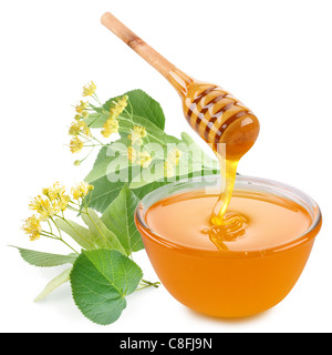 Linden honey is pouring with sticks in a jar. Next to them are linden flowers. Isolated on white background. Stock Photo