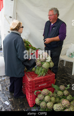 Elderly woman buying artichokes in stall at street market show Italy Italian Mediterranean Stock Photo