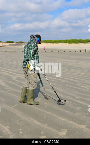 Man with metal detector  looking for lost valuables  on West Wittering beach  after the weekends crowds had departed - West Sussex, England,UK Stock Photo