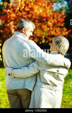 Rear view of aged man and woman taking a walk in autumnal park