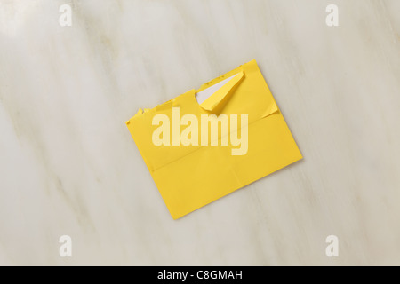 A used and slightly torn open postal envelope on a marble surface Bright yellow colored envelope Stock Photo