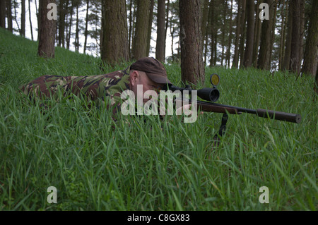 Man lying in the long grass watching and waiting with a .22 rifle in Weardale in County Durham Stock Photo