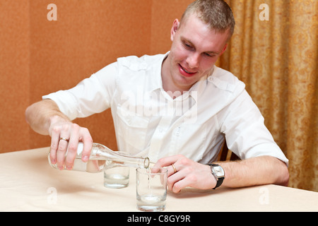 Drunken young man pouring vodka from the bottle in glasses. Stock Photo