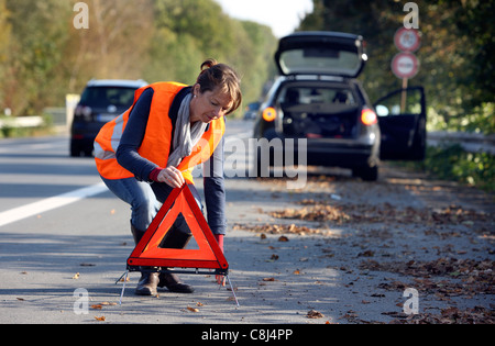 Car breakdown, on a highway, female driver, wearing a high visibility vest,  set up a warning triangle. Stock Photo