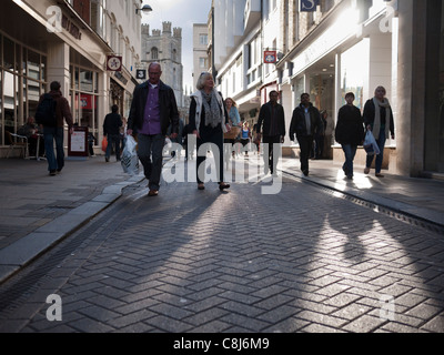 Shoppers in Cambridge walking in Market Street in backlit sunshine showing textures of road and long shadows. Stock Photo