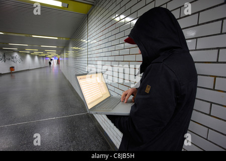 Computer user, hacker, sits conspiratorially with a laptop, in a subway station. Symbol picture, computer-Internet crime. Stock Photo
