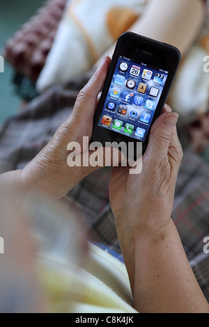 Getting to grips with smartphone 3G technology, an elderly old woman uses her iPhone to browse Facebook Stock Photo
