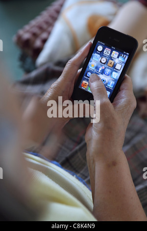 Getting to grips with smartphone 3G technology, an elderly old woman uses her iPhone to browse Facebook Stock Photo