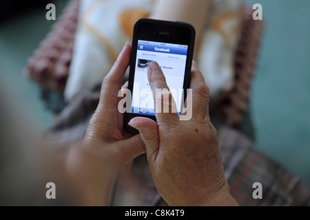 Getting to grips with smartphone 3G technology, an elderly old woman uses her iPhone to browse Facebook Stock Photo