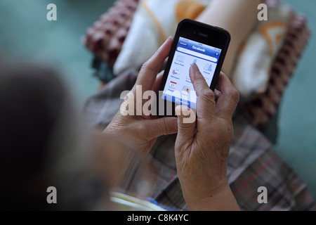 Getting to grips with smartphone 3G technology, an elderly old woman uses her iPhone to browse Facebook Stock Photo