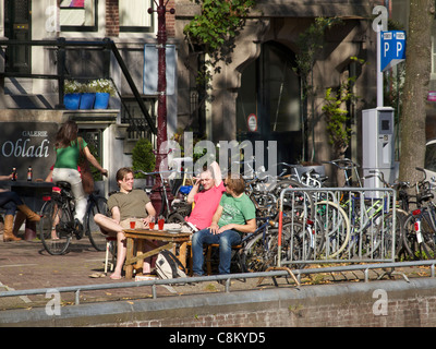 Young men students relaxing with a drink in the sunshine along a canal in Amsterdam, the Netherlands Stock Photo