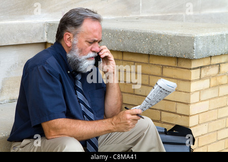 Mature unemployed salesman makes a call on his cell phone to reply to a advertisement for a want ad job in the newspaper. Stock Photo
