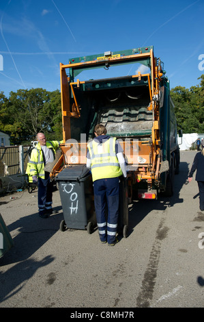 Refuse workers from Basildon Council in Essex working at rear of dust cart loading and emptying wheely (wheeled) bins into rear. Stock Photo