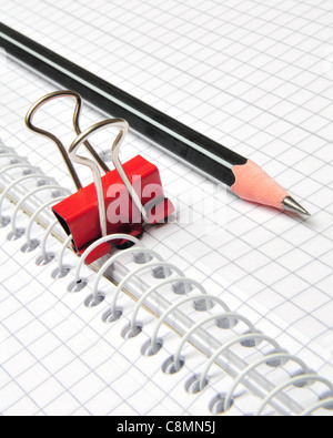 Black pencil on top of a notepad with squared paper an red clip Stock Photo