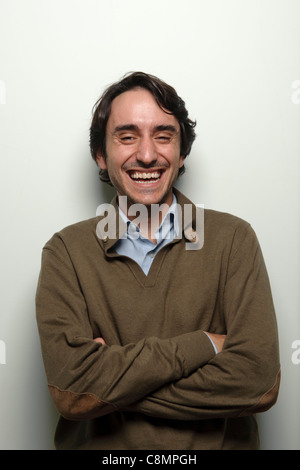 Portrait of happy young man with arms folded laughing on white background Stock Photo