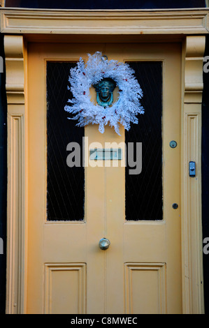 blue artificial Christmas wreath over ornate victorian style styled door knocker head figure Stock Photo