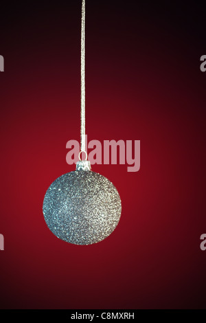 Silvery Christmas bauble on red background, blurred, with selective focus on icing. Stock Photo